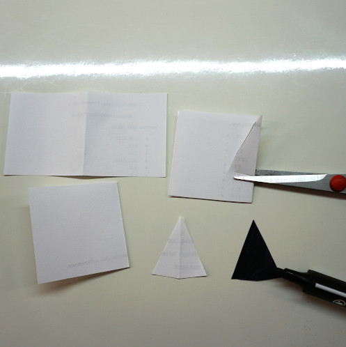 Aus einem gefalteten Papier wird ein Dreieck ausgeschnitten, aufgefaltet und schwarz angemalt